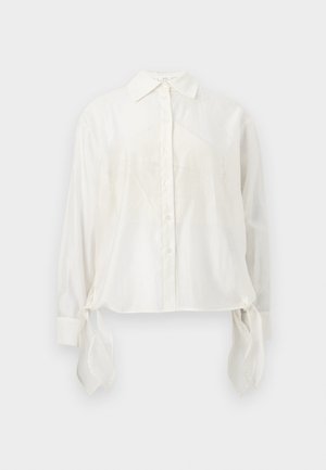 Bílá košile s dlouhým rukávem a knoflíky, se špičatým límečkem a látkovými stužkami visícími z každého manžetu, zobrazena na neutrálním pozadí.