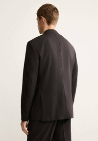 Blazer nero su misura realizzato in tessuto liscio, con colletto classico, apertura singola sul retro e spalle strutturate.