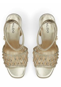 Zlaté sandály s texturovaným svrškem a tkaným vzorem, ozdobené kovovými korálky. Čtveratá špička a řemínek na kotníku s nastavitelnou sponou.