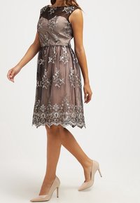Bezramenné šaty po kolena v tlumené šedé barvě s černou síťovinou. Obsahují stříbrnou květinovou výšivku a vlnkovaný lem.