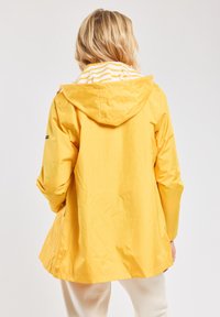 Veste imperméable jaune avec capuche, dotée d'une doublure intérieure rayée et d'une coupe ample. Texture lisse et design mi-long.