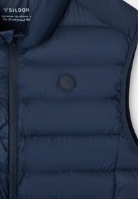 Chaleco sin mangas acolchado de color azul navy con cremallera frontal, cuello alto y pequeño logo circular en el lado izquierdo del pecho.