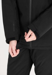 Schwarze isolierte Jacke mit durchgehendem Reißverschluss und mit Klettverschluss verstellbaren Bündchen. Mit strukturiertem Stoff und WPRO 10000-Logo auf dem Ärmel.