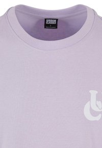 Levandulové tričko vyrobené z bavlněného materiálu. Má kulatý výstřih a bílou grafickou nálepku vpředu. Měkká textura s hladkým povrchem.