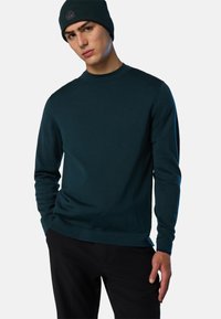 Dunkelblauer Strickpullover mit Rundhalsausschnitt und langen Ärmeln, kombiniert mit einer passenden Mütze mit einem Logopatch. Schickes und tailliertes Design.