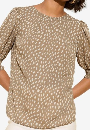 Brązowa bluzka z subtelnym, białym, nieregularnym wzorem w kropki. Posiada okrągły dekolt i bufiaste, krótkie rękawy. Gładki, lekki materiał.