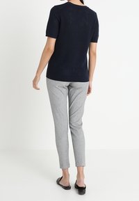 Haut en tricot texturé bleu marine à manches courtes associé à un pantalon gris clair fuselé et des chaussures plates noires. Présente un design simple et une coupe décontractée.