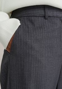 Šedé pruhované kalhoty s hladkou texturou a bočními kapsami. Pas je upravený a doplněný o svetřík z lehkého pleteného materiálu.
