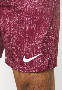 Körsbärsröda sportshorts med en texturerad mönstring och en vit Nike-logotyp på nedre vänster sida. Tillverkade av ett lättviktigt tyg.