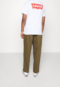 Bílý tričko s červeným logem "Levi's" na zádech, spárované s olivově zelenými kalhotami a bílými teniskami s černými akcenty.