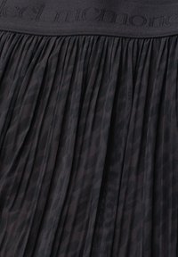Black pleated fabric with a ribbed waistband featuring subtle raised text across the top edge.