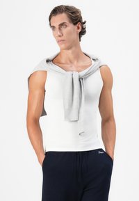 Weißes Tanktop, grauer Pullover locker über die Schultern gelegt, dunkelblaue Hose mit weißem Text. Glatter Stoff, figurbetontes Design, einfarbige Farben und lässiger Stil.