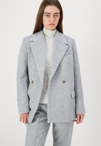 Vaaleanharmaa kaksirivinen bleiseri, joka on valmistettu teksturoidusta villasta. Siinä on kultaketjut, lovetut kaulukset ja etutasku. Slim fit -malli.