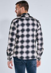 Schwarz-weiße Karoshemd mit langen Ärmeln, klassischem Kragen, durchgehender Knopfleiste und strukturiertem Stoff. Auffälliges Karomuster mit lockerer Passform.