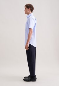 Jasnoniebieska koszula z krótkim rękawem i kieszonką na klatce piersiowej, zestawiona z ciemnymi spodniami i czarnymi butami, prezentowana na męskiej sylwetce w profilu.