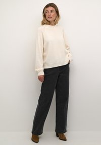 Light beige knit sweater with a crew neckline, paired with high-waisted dark gray wide-leg jeans and brown ankle boots. Smooth texture.