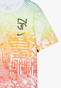 Camiseta de manga corta Nike Dri-Fit con un patrón en degradado de verde a naranja, con un logo negro y texturas geométricas en todo su diseño.
