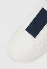 Pantof sport alb cu finisaj din piele netedă, având o bandă textilă bleumarin pe mijloc și detalii subtile de cusături.