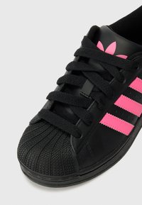Fekete sneaker szintetikus bőrből, három rózsaszín csíkkal, texturált gumi orral és fekete cipőfűzővel.