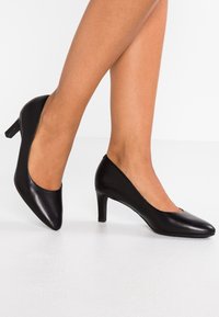 Des chaussures à talons hauts en cuir noir présentent un design à bout pointu, une texture lisse et un talon effilé. Les côtés sont légèrement découpés pour un look épuré.