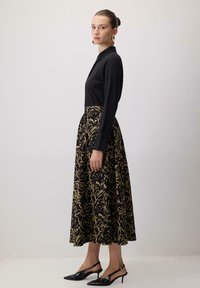 Črna dolga majica z dolgimi rokavi, kombinirana z zlato oblečeno, cvetličasto krilo do gležnjev. Oblečeno z črnimi slingback petkami. Gladka tekstura tkanine.