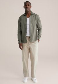 Srajca z gumbi v olivno zeleni barvi, lahkotna tkanina. Kombinirana z bež hlačami, belimi supergami in sivimi poudarki na oblačilih. Enostavna zasnova.