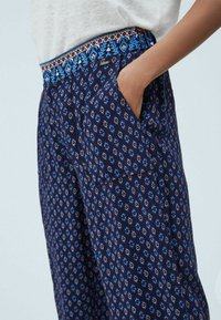 Marineblaue gemusterte Hose mit einem dekorativen elastischen Bund, der blaue, rote und weiße Akzente hat; mit seitlichen Taschen und einem lässigen Schnitt.