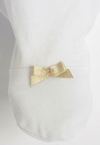 Tessuto di cotone bianco con una texture a righe, caratterizzato da un'applicazione in metallo dorato a forma di fiocco sul polsino. Design semplice e pulito.