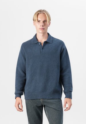 Navy blue pullover made of soft, textured fabric. Features a collar and three-button placket. Relaxed fit with ribbed cuffs and hem.