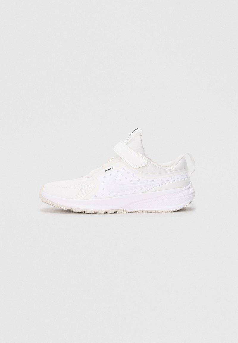 Baskets de sport blanches avec une sangle velcro, tige respirante, semelle texturée et un tirette au talon, présentées de profil.