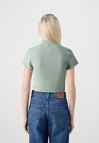 Top corto de manga corta en material de canalé verde claro, combinado con jeans de mezclilla azul de tiro alto que cuentan con una etiqueta de marca en la parte posterior.