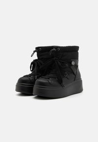Black ankle boots with a padded upper, round toe, thick platform sole, and front lacing. Features metal grommets and elastic accents.