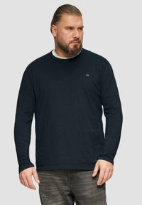 Langarmiges navy-blaues T-Shirt aus weichem Stoff mit rundem Halsausschnitt und kleinem Logo auf der Brust, kombiniert mit verwaschenen grauen Jeans.