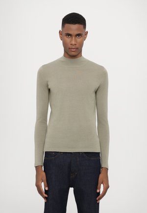 Pull à col roulé vert clair à manches longues en tricot doux et ajusté avec une texture lisse. Assorti à un jean en denim bleu foncé.