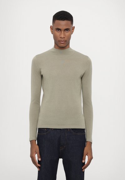 Maglione turtleneck verde chiaro a maniche lunghe, realizzato in un tessuto maglia morbido e aderente con una texture liscia. Abbinato a jeans in denim blu scuro.