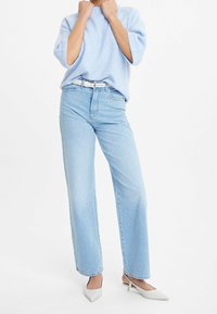 Maglione azzurro chiaro con vestibilità ampia e maniche corte, abbinato a jeans azzurri chiari a vita alta. Accessori includono una cintura bianca e scarpe bianche a punta.