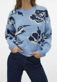Světle modrý pletený svetr s námořnickým květinovým vzorem, s žebrovanými manžetami a lemem. V kombinaci s tmavě modrými džíny, které mají pohodlný střih.