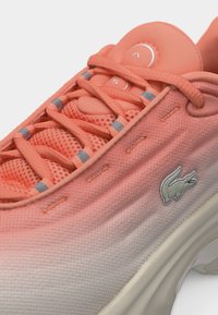 Baskets dégradées corail et blanc avec dessus en maille, lacets, œillets réfléchissants et logo crocodile brodé sur le côté.