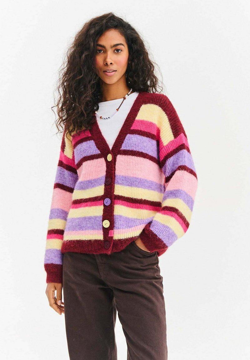 Kolorowy sweter na drutach z pionowymi paskami w różowym, żółtym, fioletowym i bordowym kolorze. Posiada dekolt w serek i cztery guziki.