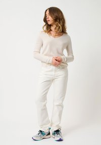 Maglione beige chiaro a scollo a V, jeans bianchi a gamba dritta e sneakers grigie con accenti turchesi e viola. Tessuto liscio, design aderente.