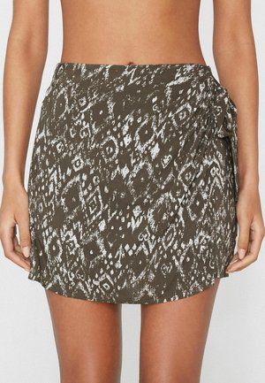 Vue de la taille jusqu'au milieu de la cuisse d'une personne portant une jupe portefeuille à motifs marron et blanc avec un lien sur le côté.