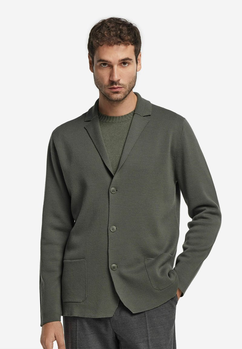 Grön stickad blazer med en strukturerad yta, har en slagkrage, två framfickor och tre knappar fram.
