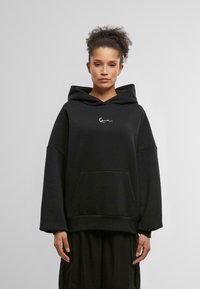 Zwarte oversized hoodie met een voorzak, voorzien van een klein wit logo op de borst. Gladde stof, relaxte pasvorm en een capuchon met trekkoord.