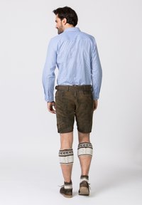 Shorts en cuir marron, chemise à carreaux bleue et jambières en tricot blanches. La tenue comprend une ceinture avec une boucle simple et des chaussures à cheville.