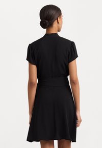 Svart klänning med korta puffärmar och en figursydd midja, med en utsvängd kjol. Tillverkad av ett slätt tyg, minimalistisk design.