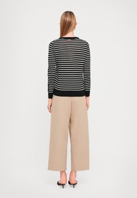 Pull rayé noir et blanc à manches longues avec des accents de boutons, associé à un pantalon large beige et des mules à talons noires.