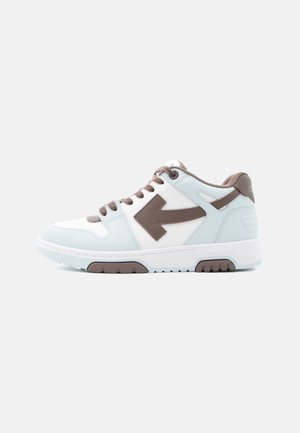 Baskets basses avec panneaux blancs et bleu clair, lacets marron, accents de semelle, et un grand motif flèche marron sur le côté.