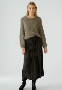 Pull en laine marron duveteux avec un col rond et des manches longues, associé à une jupe plissée noire et des bottes noires jusqu'au genou.