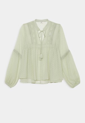 Jasnozielona bluzka z długimi, bufiastymi rękawami, z fakturą w kropki i koronkowym wykończeniem. Posiada wiązanie przy dekolcie oraz luźny, zwiewny krój.
