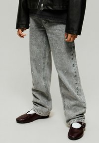 Hallid hallid denim teksad lõdva lõikega, millel on väikesed dekoratiivsed nupukesed. Koos tumepunaste lamedate jalanõude ja valgete sokkidega.